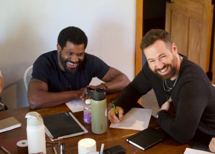 Two men laughing over their notebooks at the retreat table