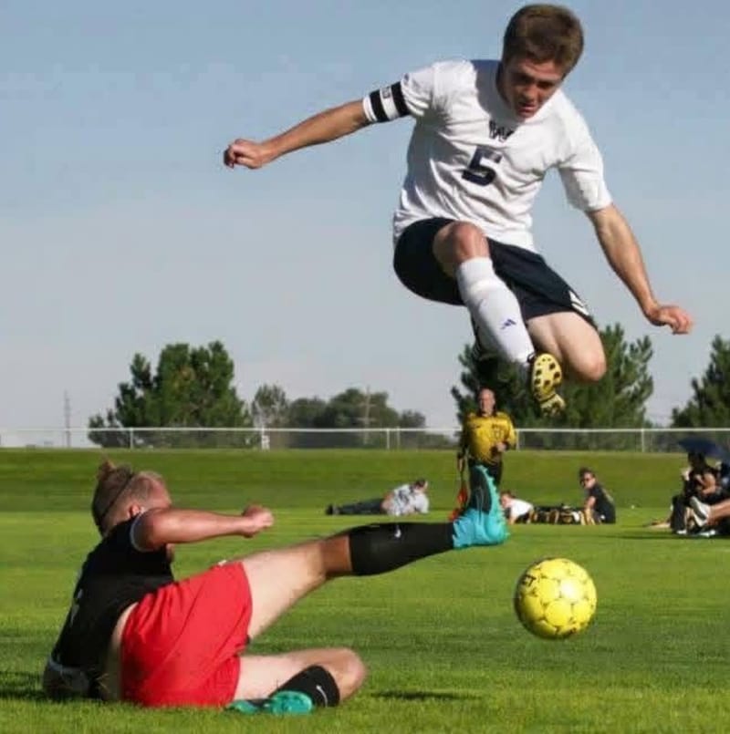 A young soccer player leaping over a sliding defender to reach the ball